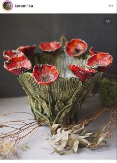 some red flowers are in a vase on a white tablecloth with dried plants and twigs