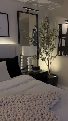 a white bed sitting under a large mirror next to a plant in a vase on top of a table