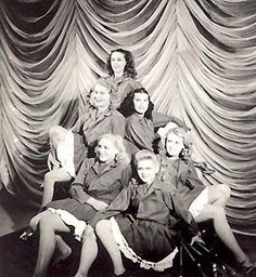 a group of women sitting on top of a chair in front of a stage curtain