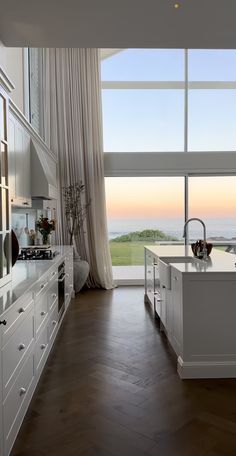 a large kitchen with white cabinets and wood flooring next to a window overlooking the ocean