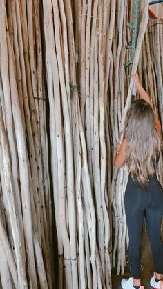 a woman standing in front of a wall made out of sticks and wood planks