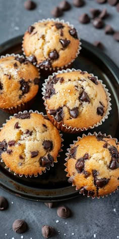 chocolate chip muffins on a black plate with chocolate chips scattered around the edges