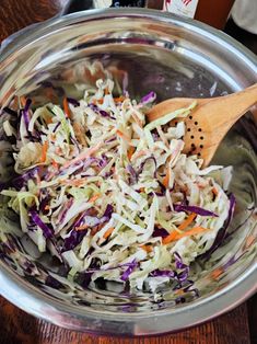 a wooden spoon in a bowl filled with coleslaw