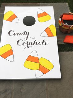 a cornhole board sitting on the ground next to an orange and yellow striped hat