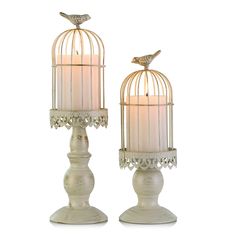 two white birdcages sitting on top of each other next to a lit candle