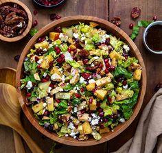 a wooden bowl filled with salad next to two bowls of dressing and spoons on a table