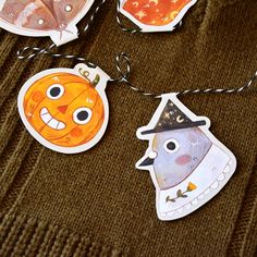 three halloween tags are hanging from a string on a brown sweater with two orange pumpkins