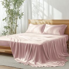 a bed with pink sheets and pillows in a room next to a potted plant