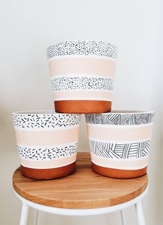 four planters sitting on top of a wooden table next to a white wall with black and white designs