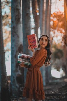 a woman in an orange dress is holding up a book while standing in the woods