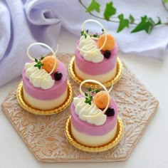 three small desserts are sitting on a gold platter with white and pink icing