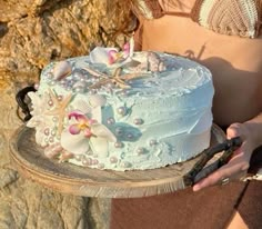 a woman holding a cake with flowers and pearls on it, in front of some rocks