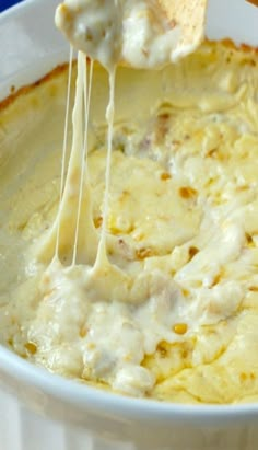 a person is dipping cheese into a bowl of dip with tortilla chips on the side