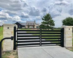 a black and white gate in front of a house with a driveway leading to it