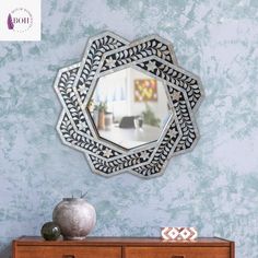 a mirror is hanging on the wall above a dresser with drawers and vases next to it