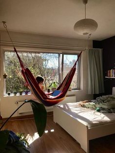 a woman sitting in a hammock on top of a bed next to a window