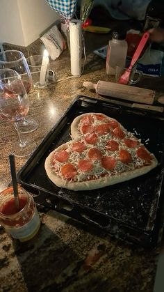 a pizza sitting on top of a pan covered in cheese and toppings next to wine glasses