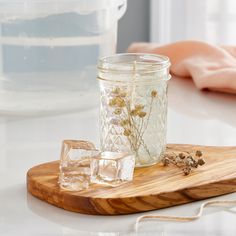 a glass jar filled with ice cubes on top of a wooden tray next to a container