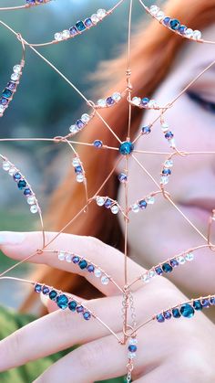 a woman is holding up some kind of wire structure with blue beads and crystals on it