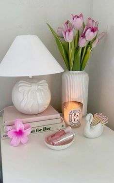 a white table topped with books and a lamp next to a vase filled with pink flowers