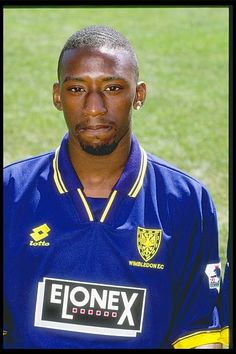 a man in a blue uniform is posing for a photo on the soccer field with grass behind him