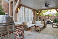 an outdoor living area with couches, tables and grilling oven in the background