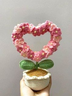 a hand holding a crocheted heart shaped object with flowers on it's top