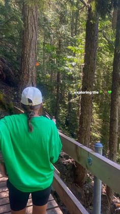 a woman in green shirt and black shorts on wooden walkway next to forest with trees