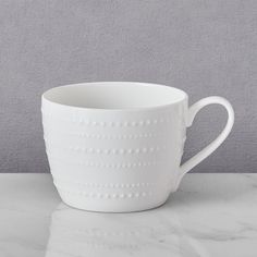 a white coffee cup sitting on top of a marble counter next to a gray wall