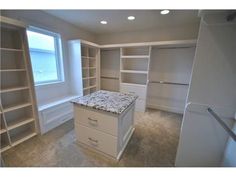 an empty walk in closet with granite counter top and white shelving unit behind it