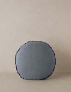 a gray pillow with scalloped edges on a beige background, it looks like an oval cushion