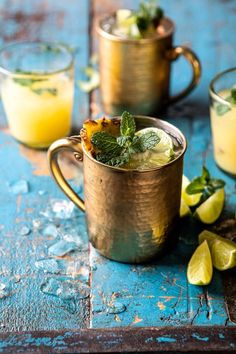 two cups filled with lemonade and mint garnish on a blue table next to limes