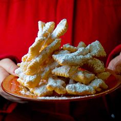 a person holding a plate full of powdered sugar coated pastry sticks in their hands