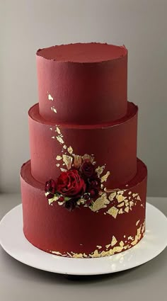 a three tiered cake with red frosting and gold leaf decoration on top, sitting on a white plate