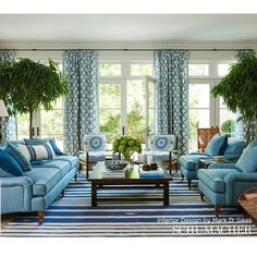 a living room with blue couches and chairs in front of two large windows that have potted plants on them