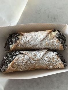 two pastries are sitting in a box on the counter top, covered with powdered sugar and blackberries