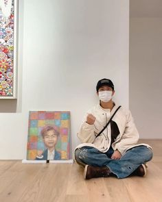 a man sitting on the floor wearing a face mask in front of some art work