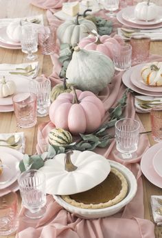 the table is set with pink and white dishes, pumpkins, and other decorations