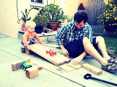 a man sitting on the ground next to a child who is playing with wooden blocks