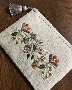 an embroidered piece of cloth with flowers and leaves on it sitting on a wooden table