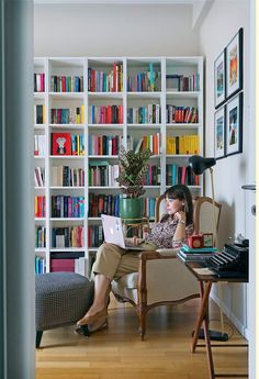 a woman sitting at a desk with a laptop in front of a bookshelf