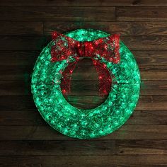 a lighted wreath with a red bow on the top and green lights around it, sitting on a wooden floor