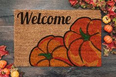 a welcome mat with three pumpkins on it and fall leaves around it, along with the words welcome