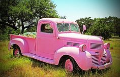 an old pink truck is parked in the grass