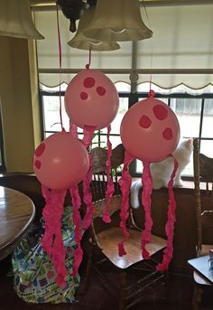 three pink balloons hanging from the ceiling in front of a window with a cat looking on