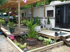 an rv is parked next to a deck with plants and flowers on it in front of the trailer