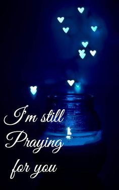 a jar filled with blue hearts sitting on top of a black table next to the words i'm still praying for you