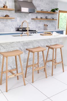 three wooden stools sit in front of an island with marble countertops and shelves