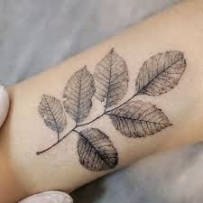 a woman's arm with a leaf tattoo on it