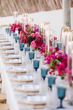 a long table is set with candles and flowers in vases, plates and napkins